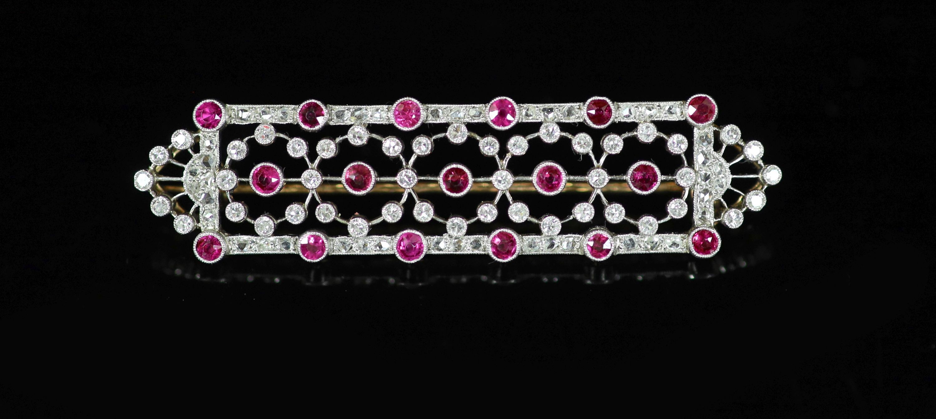 A 1920's/1930's style pierced gold and platinum, ruby and diamond chip millegrain set shaped oblong cluster brooch